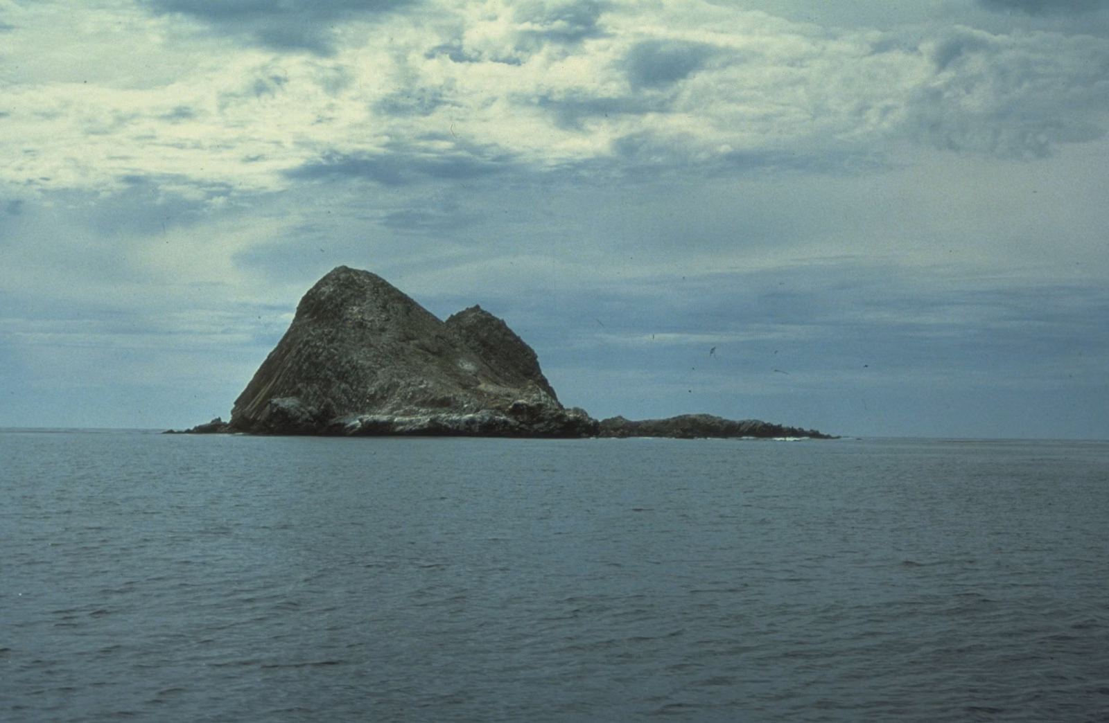 Rocky islet rising from a calm sea under clouds, Channel Islands