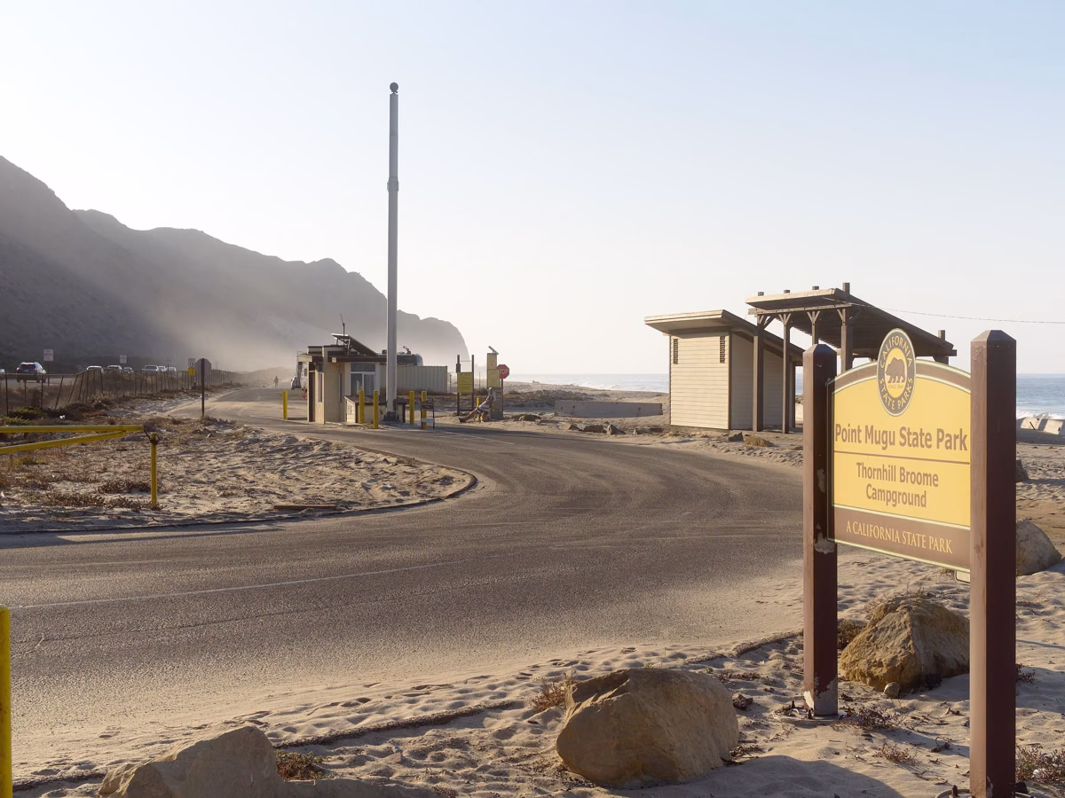 Campground entrance road with a park sign and buildings at a California state beach