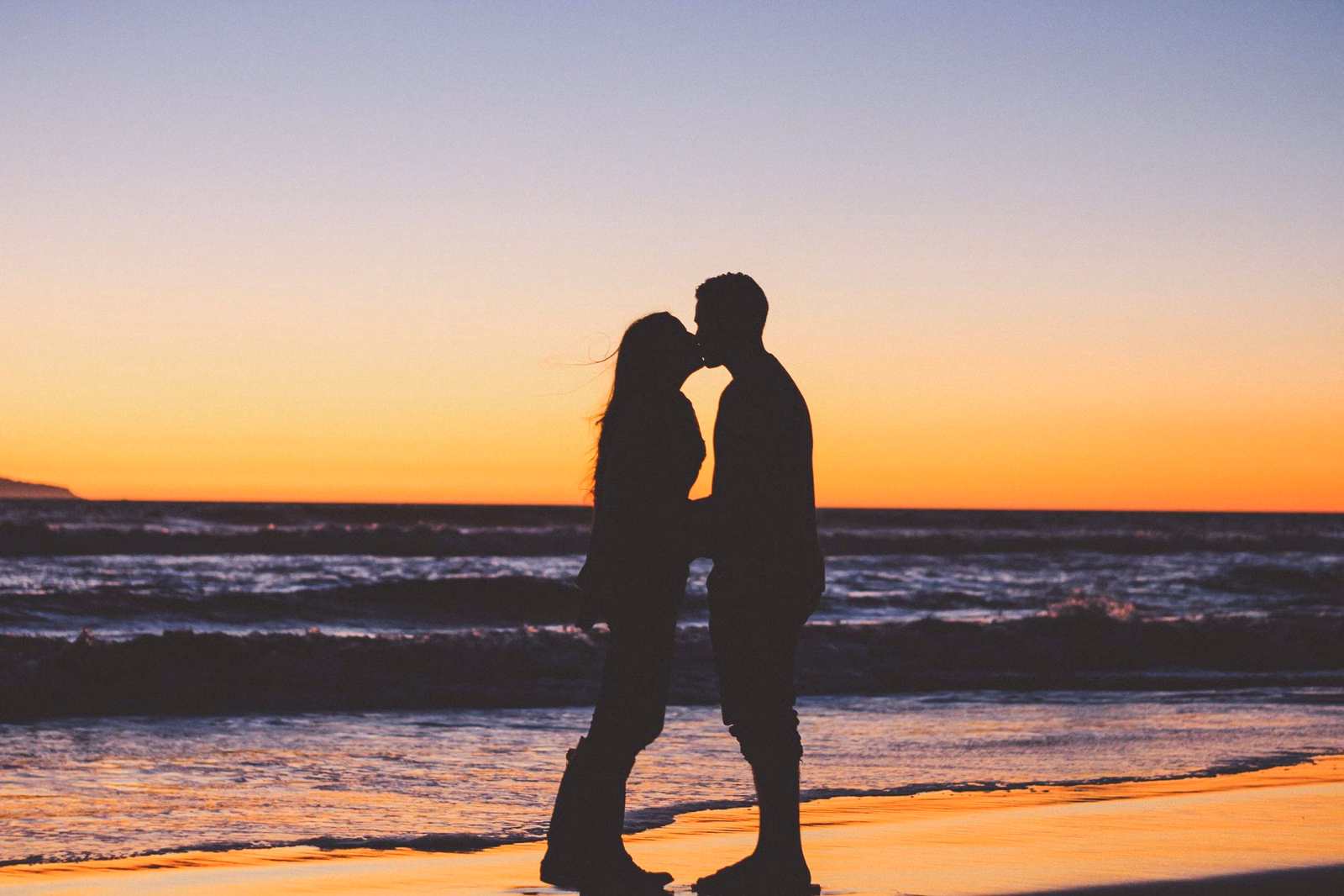 Couple silhouetted against a sunset on the beach